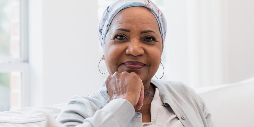 Mulher negra com lenço na cabeça encarando a câmera com um leve sorriso