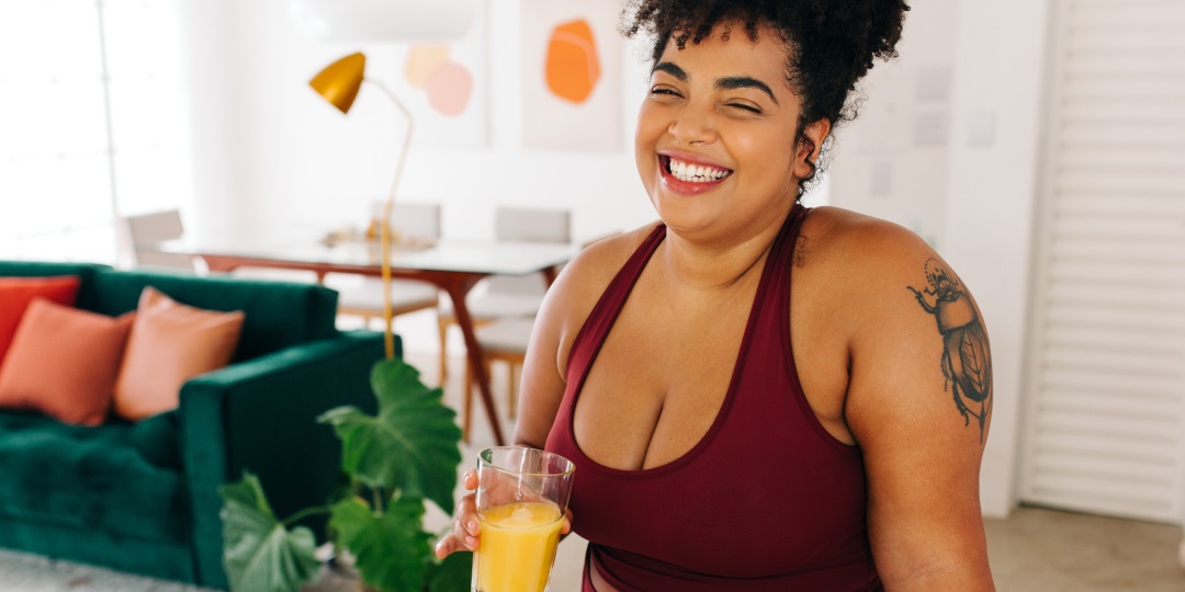 Mulher jovem negra sorrindo segurando copo de suco