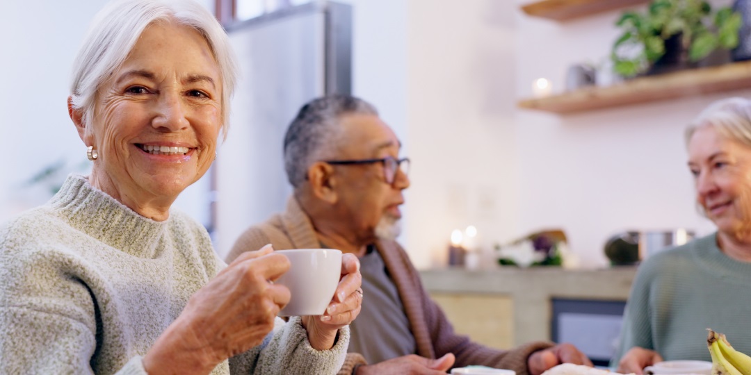 Mulher idosa toma chá com amigos, enquanto sorri