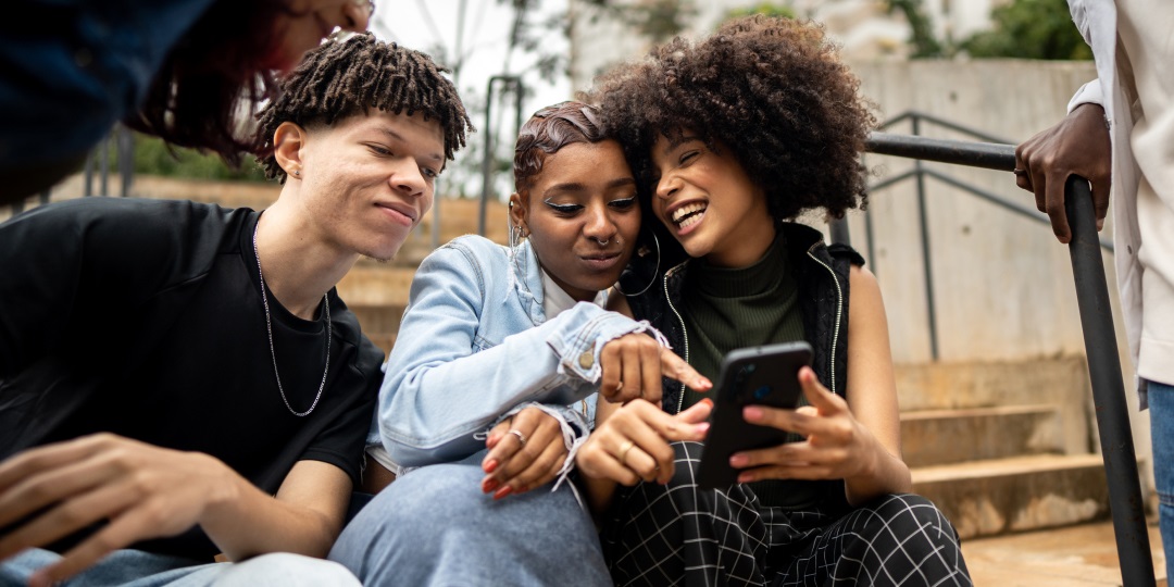 Grupo de jovens olhando para a tela do celular e se divertindo entre si