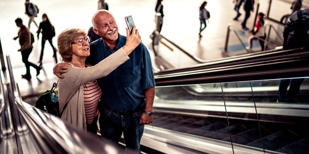 Casal de idosos na escada rolante tirando selfie no celular