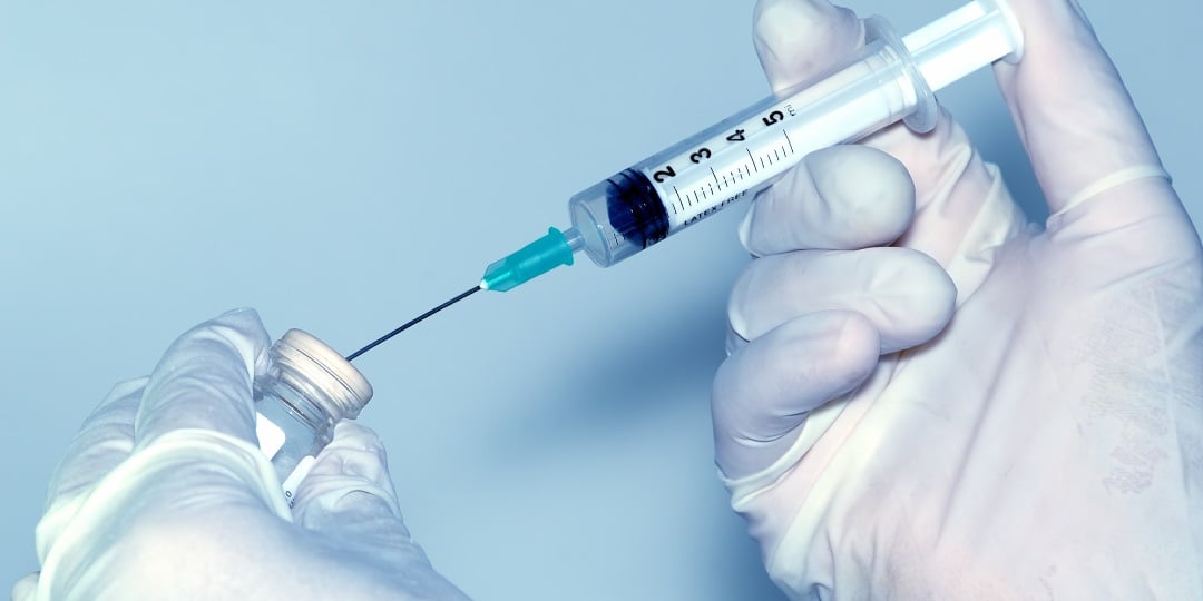 Mãos com luvas segurando seringa e ampola de vacina