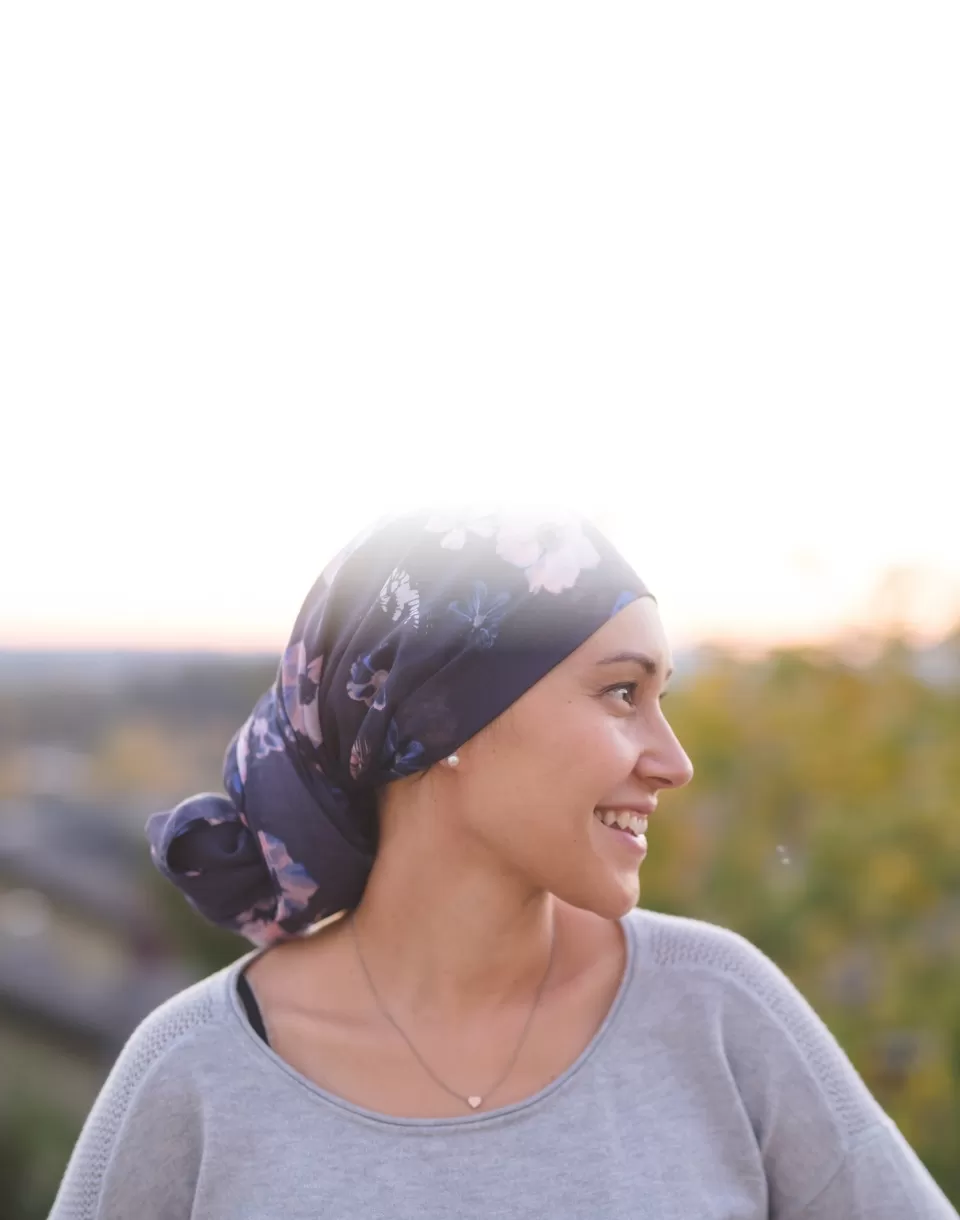 Mulher com pano na cabeça olha para o horizonte, sorridente