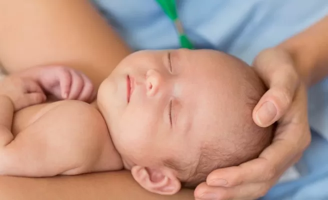 Bebê dormindo sendo segurado por mãos