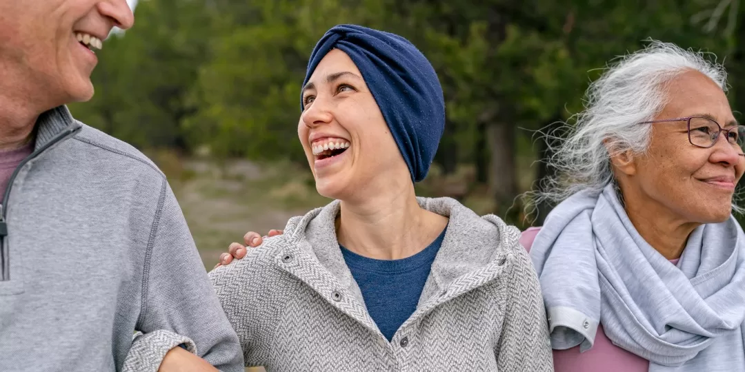 Mulher com pano enrolado na cabeça sorridente caminha abraçada em homem e mulher mais velhos