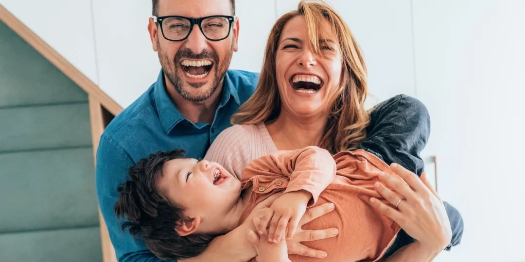 Homem e mulher seguram criança no colo, todos sorrindo