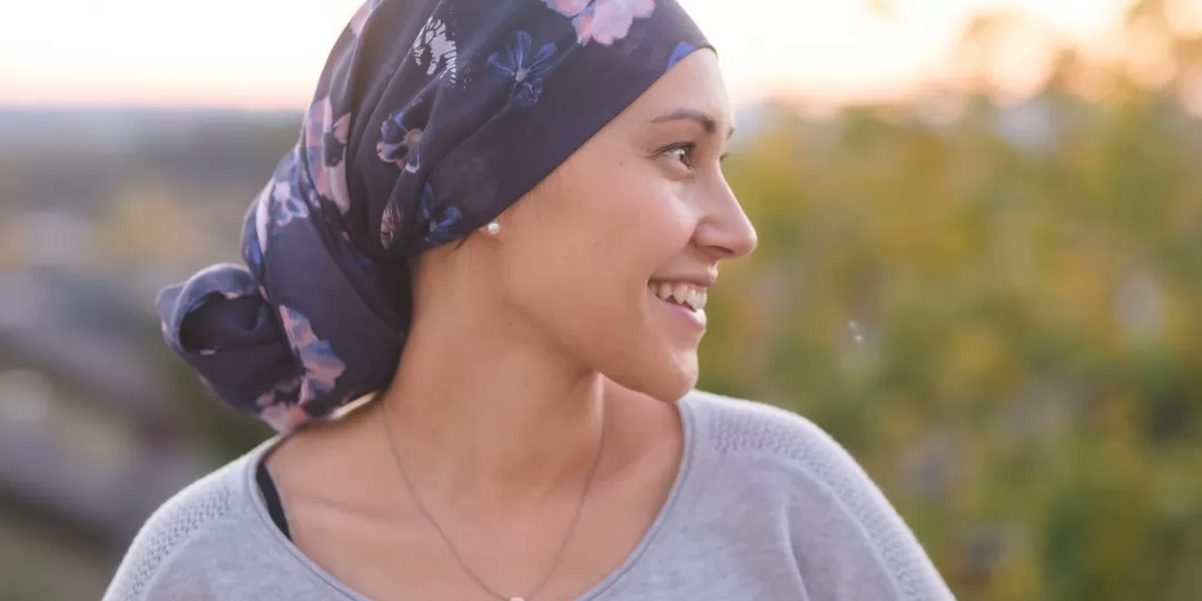 Mulher com lenço enrolado na cabeça olha para o horizonte feliz