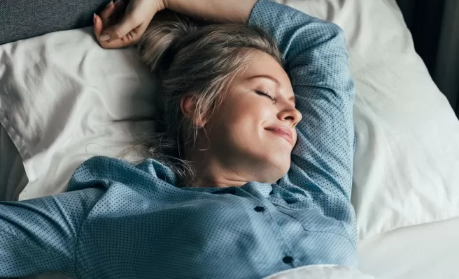 Mulher feliz se espreguiça na cama