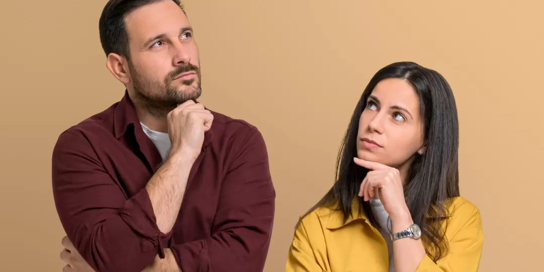 Homem e mulher brancos com mão no queixo e expressão pensativa