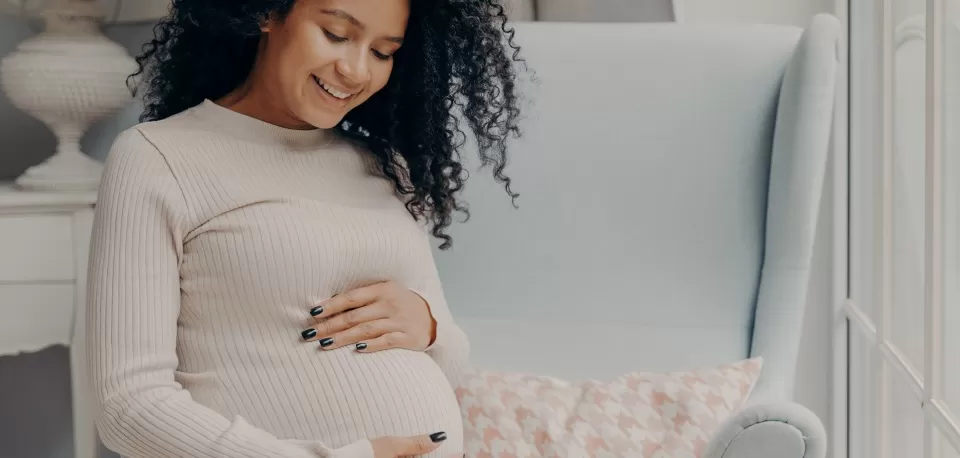 Mulher negra grávida sorridente com as mãos na barriga