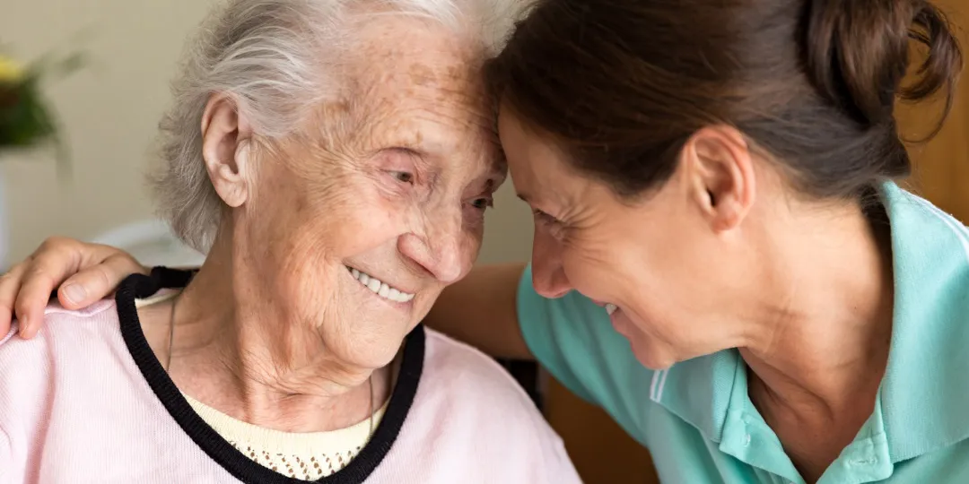 Idosa com Alzheimer e mulher se abraçam sorrindo